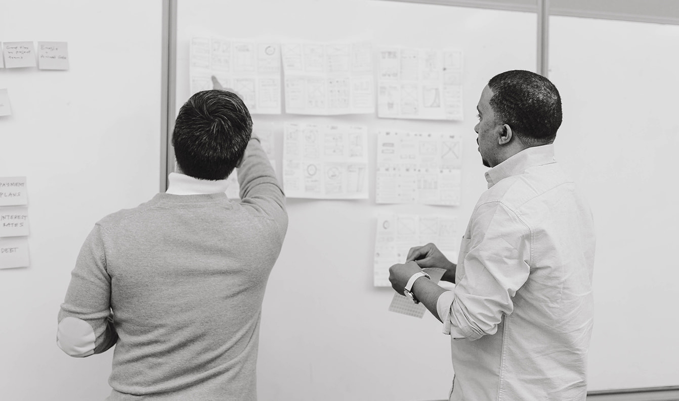 Two designers reviewing wireframe sketches on a whiteboard